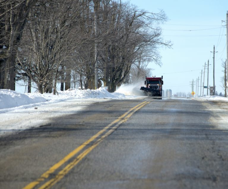 A snowplow driving down a two lane road during winter.
